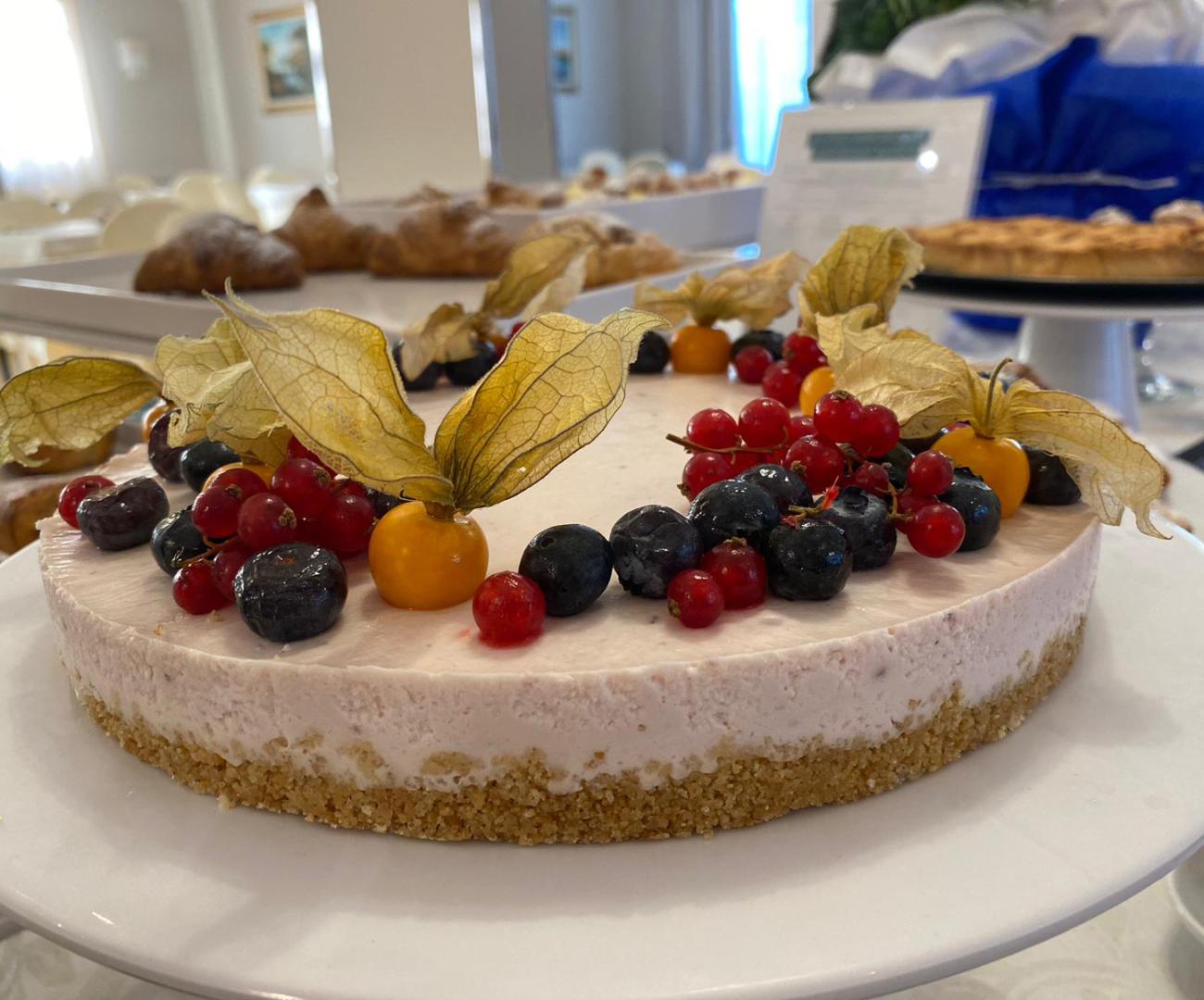 Cheesecake con frutti di bosco e alchechengi su base di biscotto.