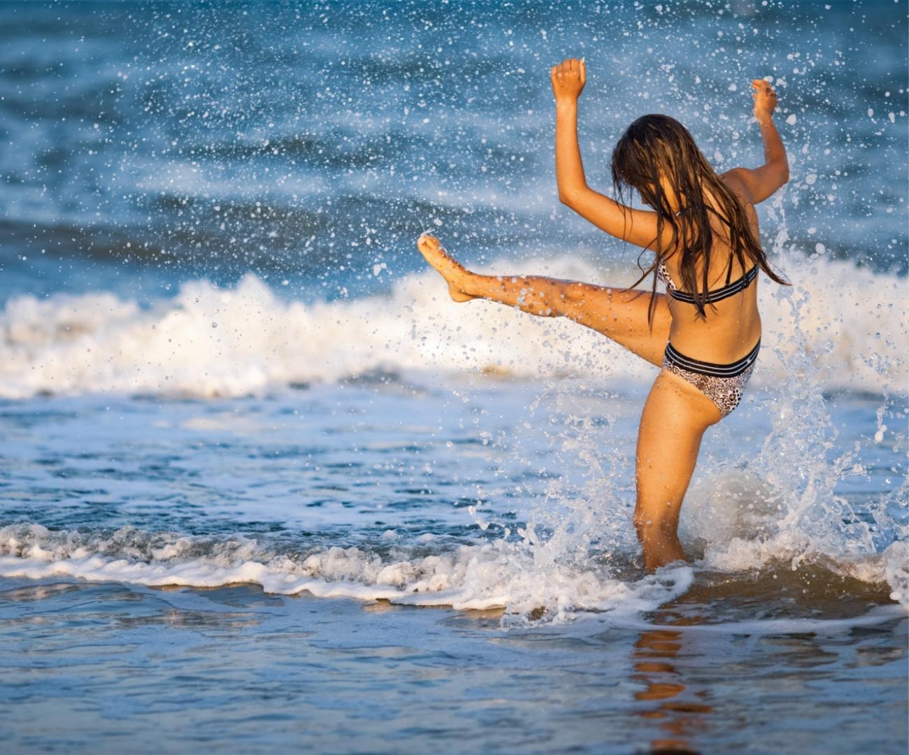 Una ragazza gioca con l'acqua sulla spiaggia, alzando una gamba.