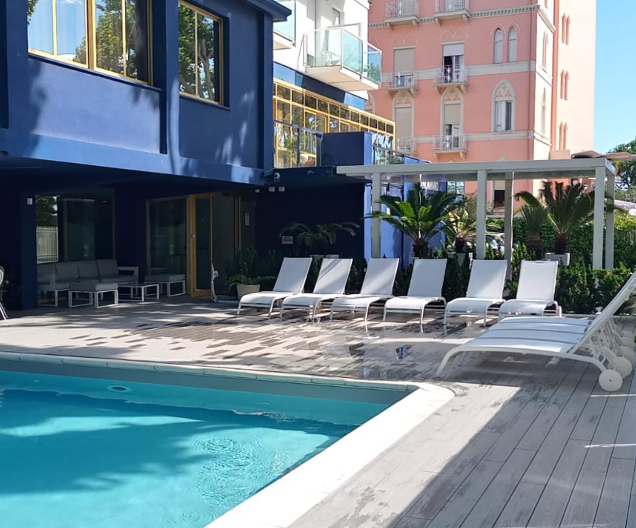 Piscina all'aperto con lettini, vicino a un edificio blu e uno rosa.