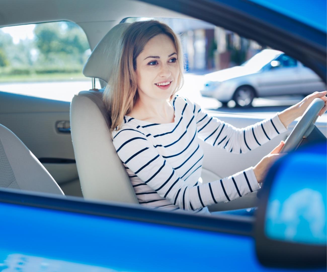 Donna sorridente alla guida di un'auto blu.