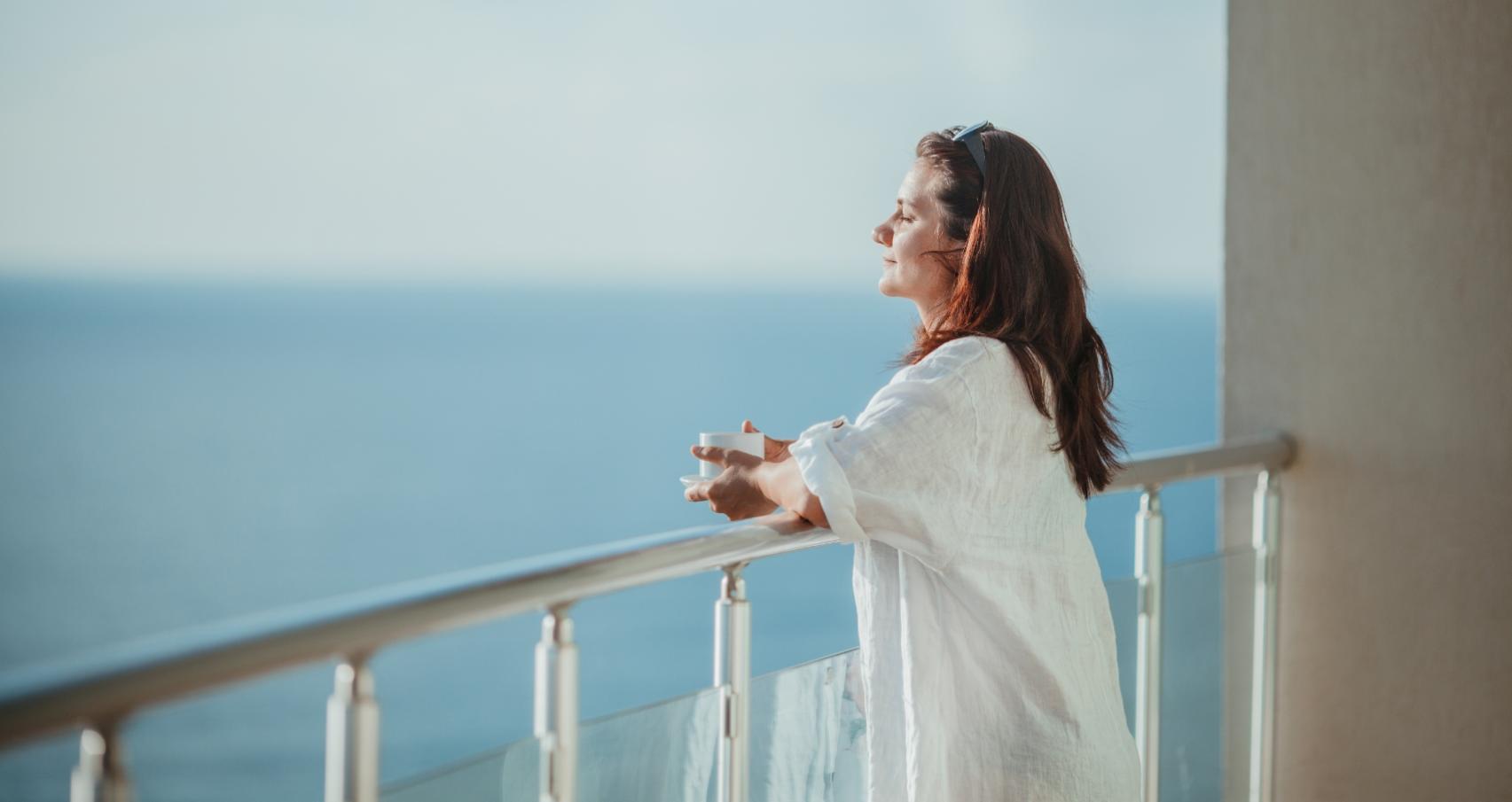 Relaxed woman on a balcony with sea view, sipping a beverage.