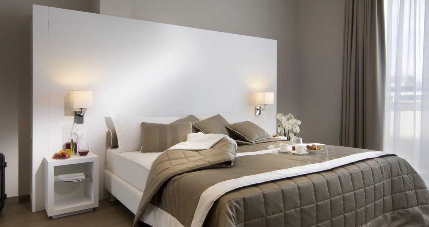 Modern room with double bed, suitcase, and breakfast on the bed.