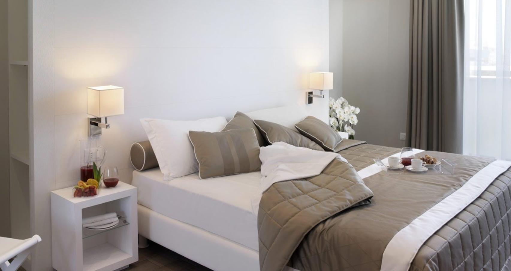 Modern bedroom with double bed, gray pillows, and breakfast on the bed.
