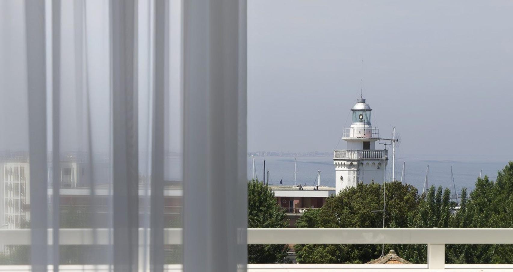 View of a lighthouse through a window with sheer curtains.