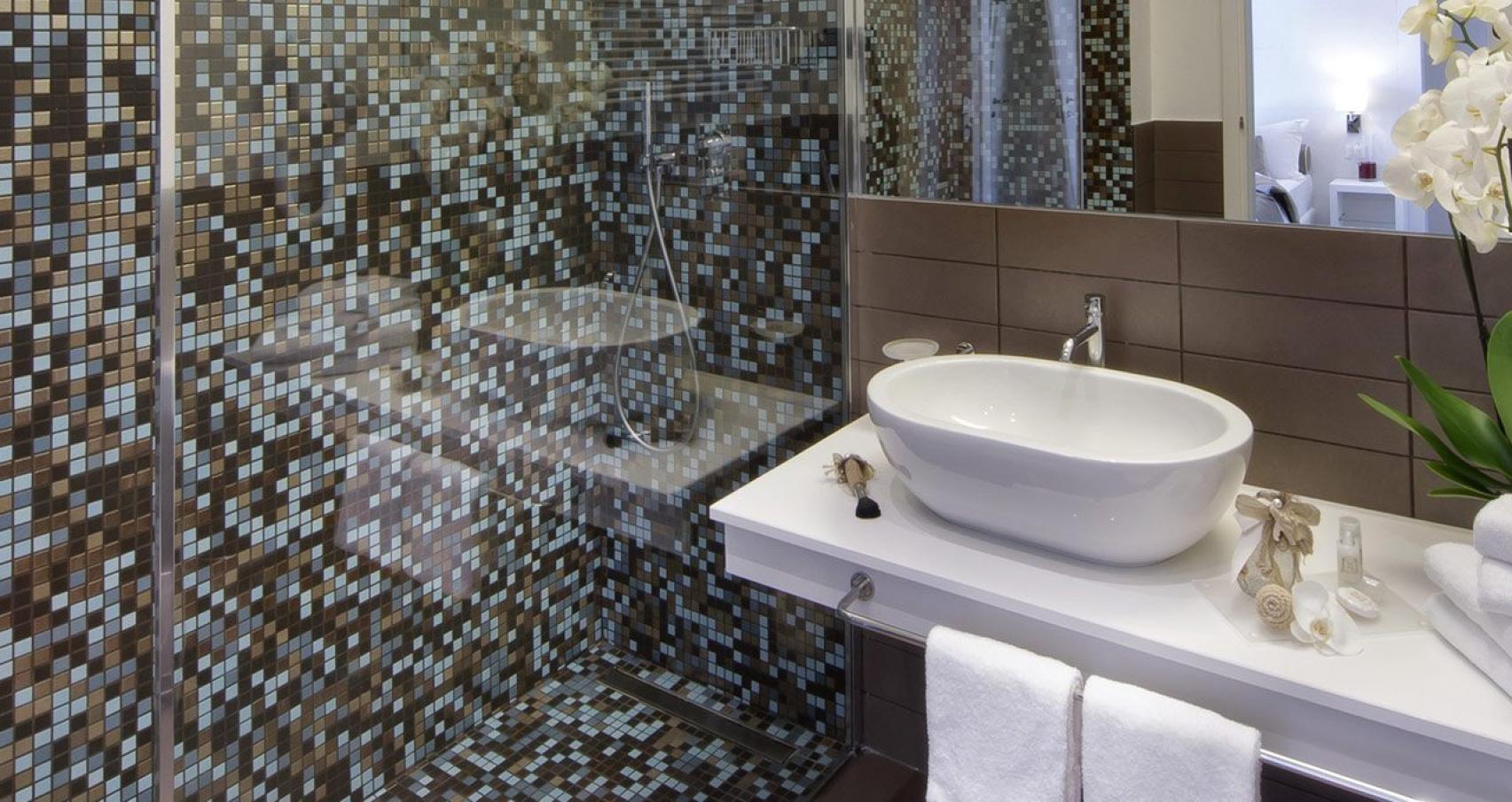 Modern bathroom with mosaic shower, white sink, and white towels.