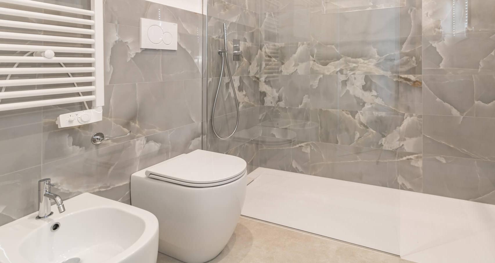 Modern bathroom with rain shower and white fixtures on marble-effect tiles.