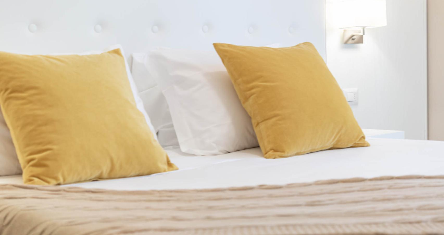 Bed with yellow pillows and beige blanket in a bright room.