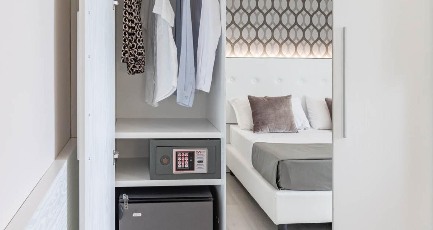Wardrobe with clothes, safe, and mini fridge in the bedroom.